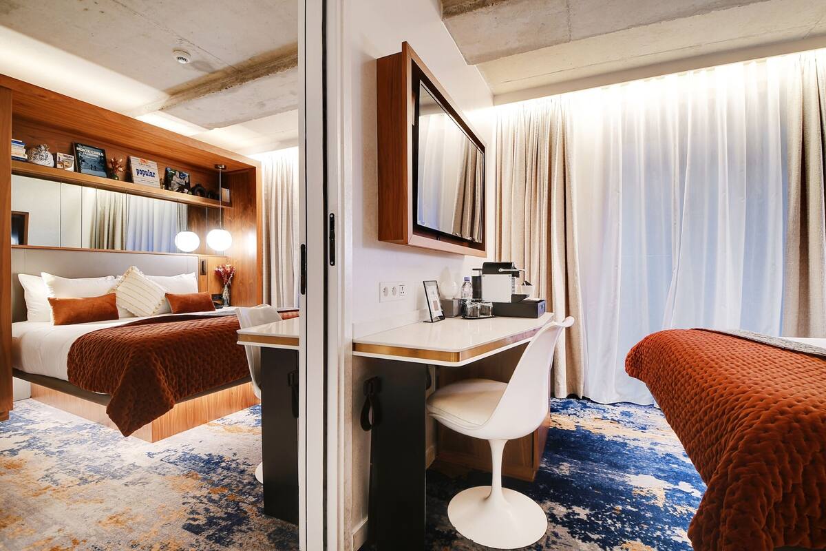 A hotel room with a bed, a desk, a chair, a mirror, and a window with curtains.