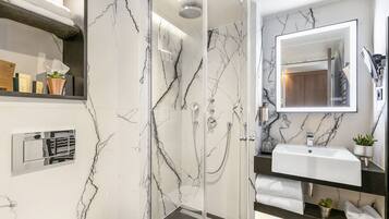 A modern bathroom with a glass-enclosed shower, a white sink, and a marble backsplash.