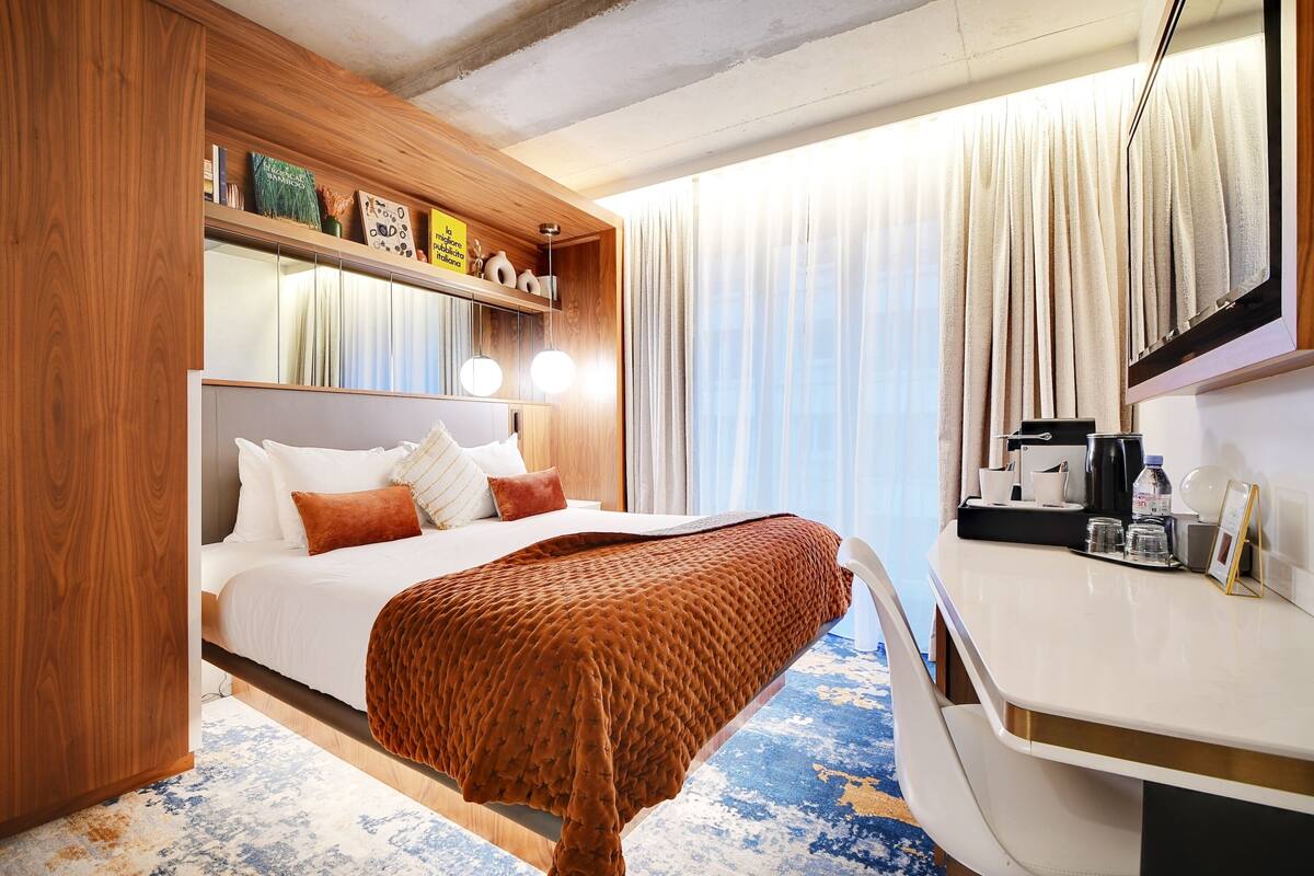 A hotel room with a bed, bedside table, and a large window with curtains.