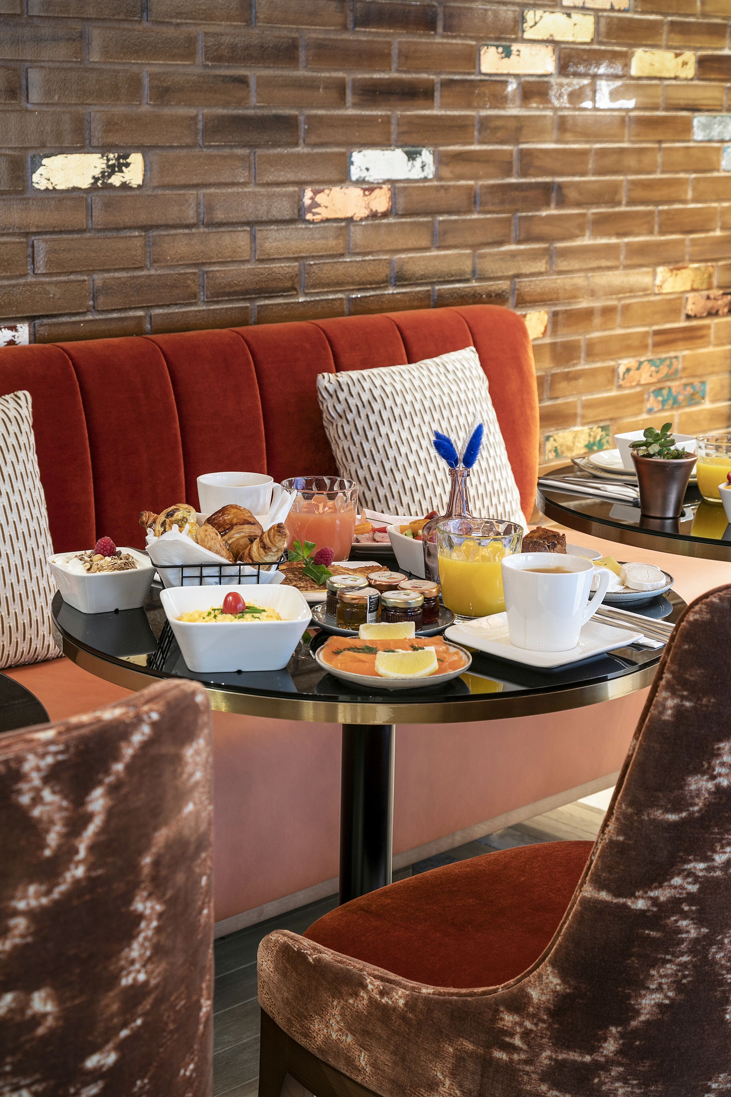 A breakfast setting with a table, red upholstered bench, and a brick wall background.