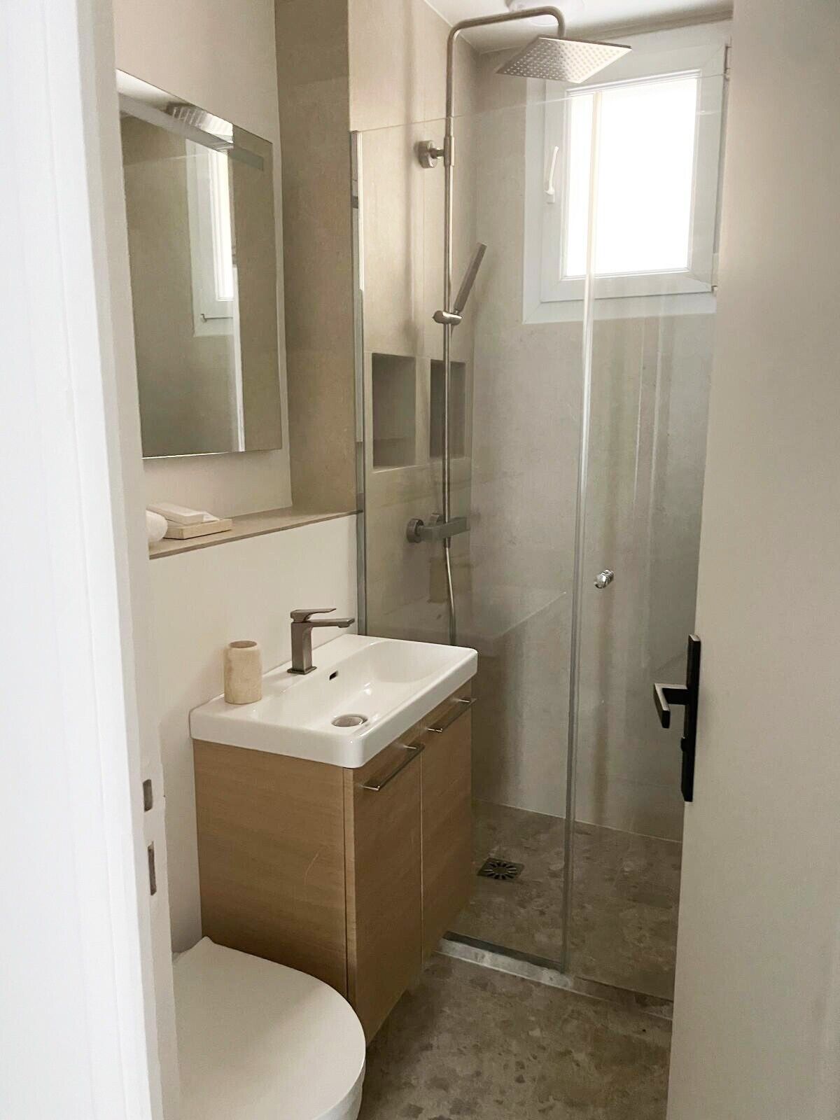 Un baño moderno con ducha envuelta en vidrio, un lavabo blanco y un espejo sobre el mueble.