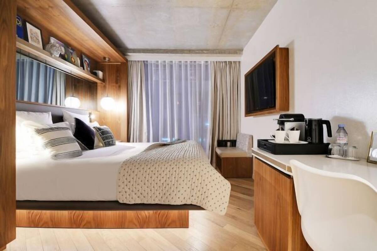 A hotel room with a bed, bedside table, TV, and a desk with a chair.