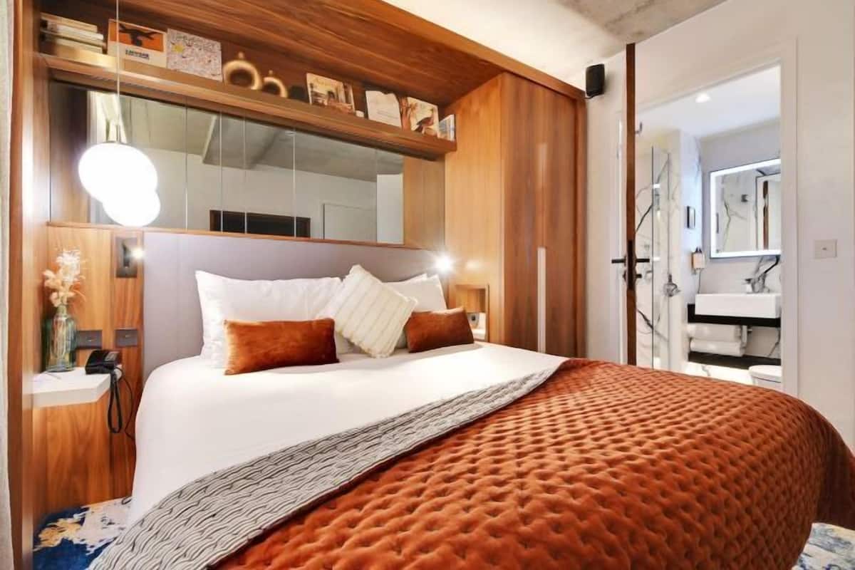 A bedroom with a large bed, a bedside table, a mirror, and a wardrobe.
