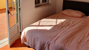 A bedroom with a bed, a window, a painting, and a view of the sea.