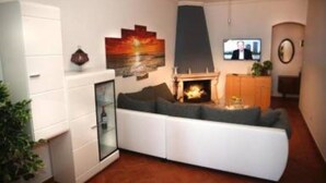 A modern living room with a white sofa, a fireplace, a TV, and a painting on the wall.