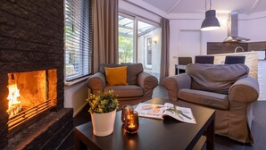 Een moderne woonkamer met een open haard, comfortabele zitplaatsen, een eethoek en een keuken op de achtergrond.