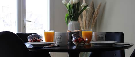 Mesa de jantar com itens de café da manhã, um vaso com flores brancas e uma janela com vista.