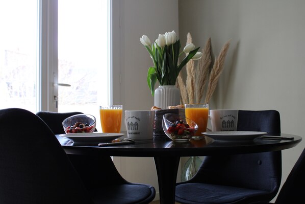 A dining table with breakfast items, a vase with white flowers, and a window with a view.