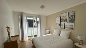 A bedroom with a large bed, a dresser, a bedside table with a lamp, and a wall with framed pictures.