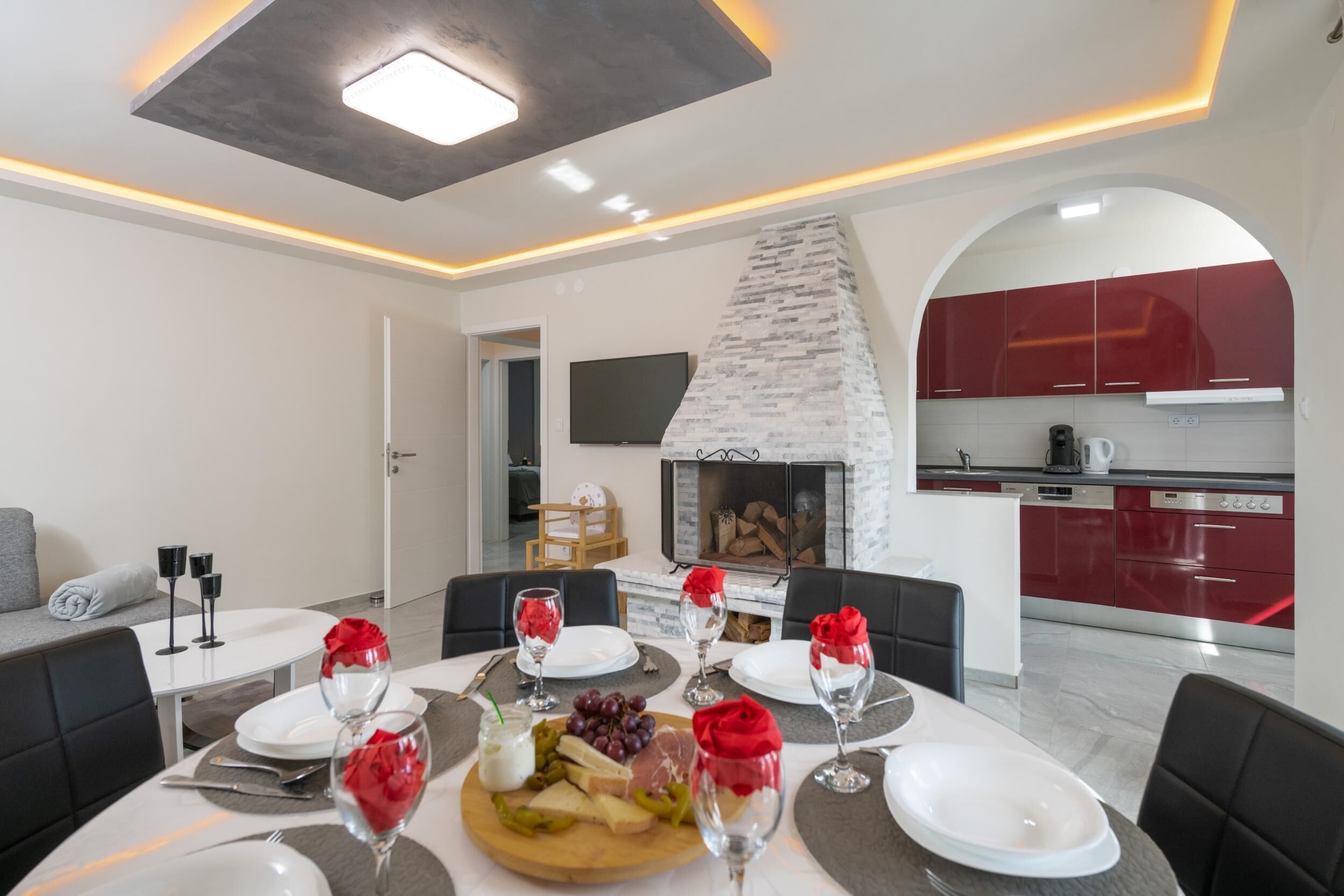A modern dining area with a fireplace, red cabinets, and a flat-screen TV.