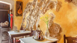 A rustic interior with exposed stone walls, a wooden table with a tray of coffee beans, a traditional tea set, and a hanging guitar.