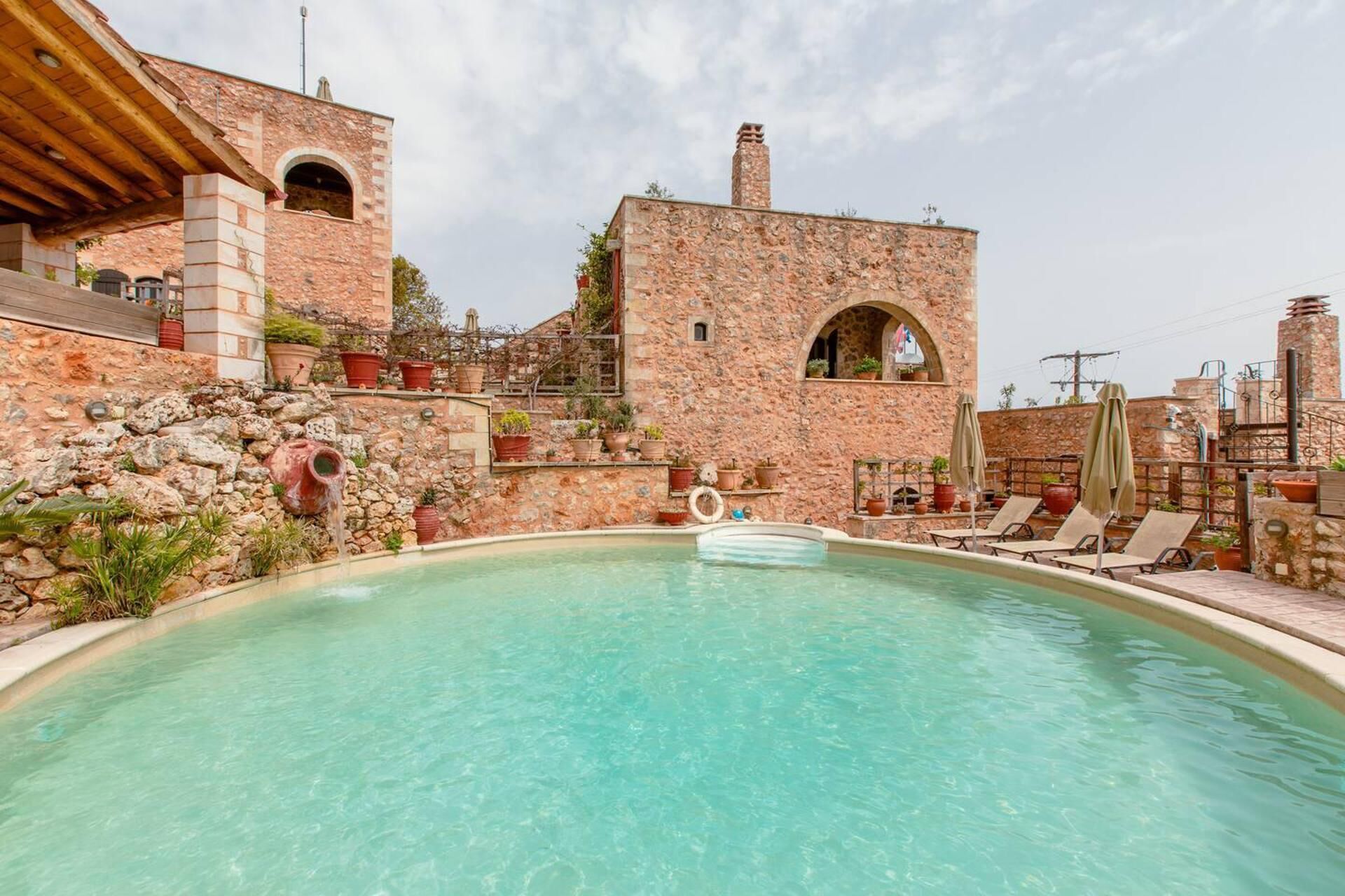 A pool area with a stone building, lounge chairs, and potted plants.