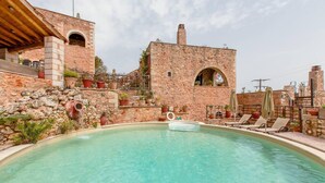 A pool area with a stone building, lounge chairs, and potted plants.