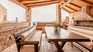 An outdoor patio with wooden furniture, a stone wall, and a view of the landscape.