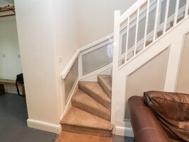 A staircase with carpeted steps, white walls, and a brown leather couch in the foreground.