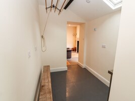 A narrow hallway with a wooden bench, a ceiling light fixture, and a door leading to a room with a dark floor.