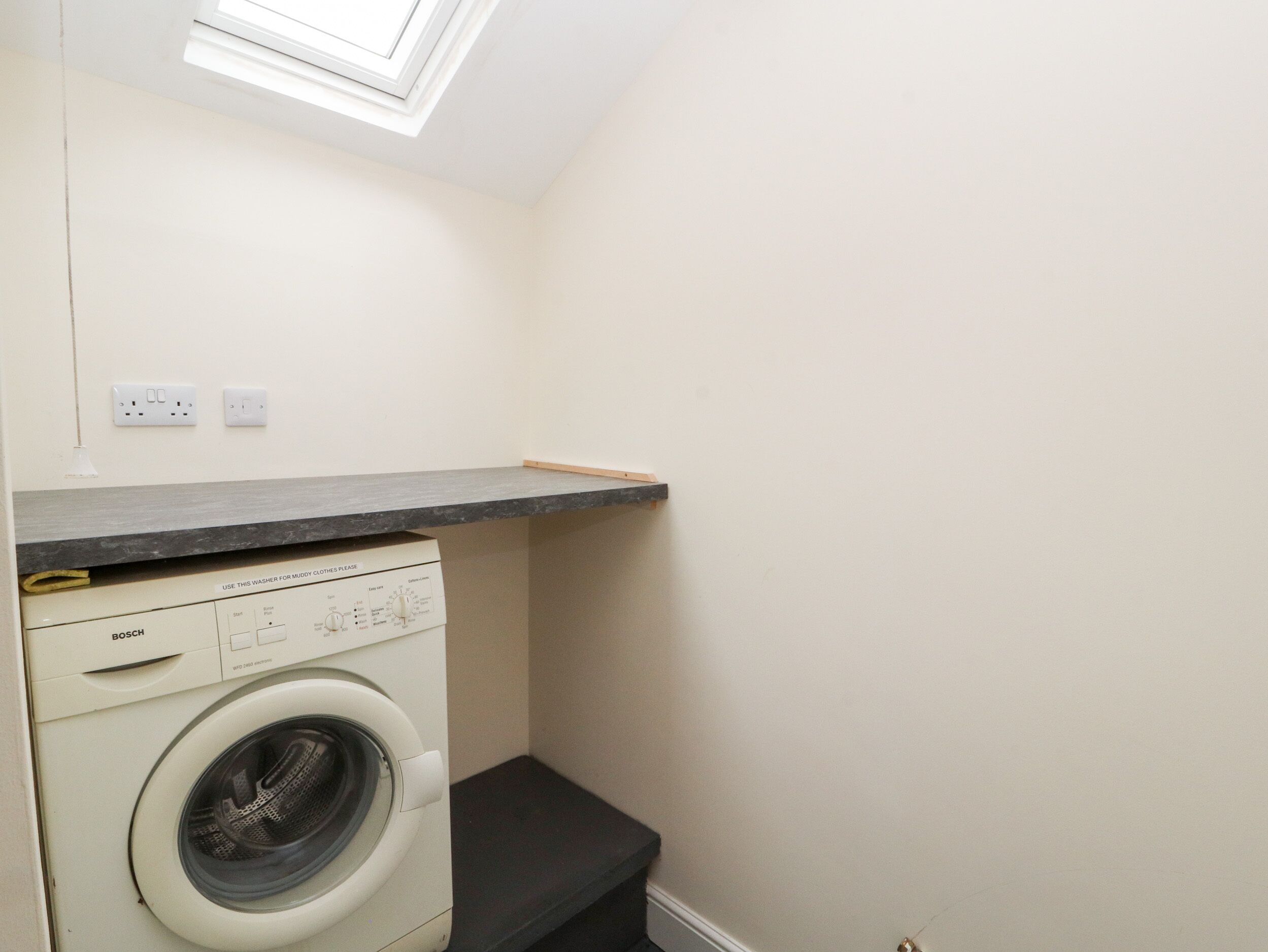 A compact laundry room with a Bosch washing machine, a countertop, and a skylight.
