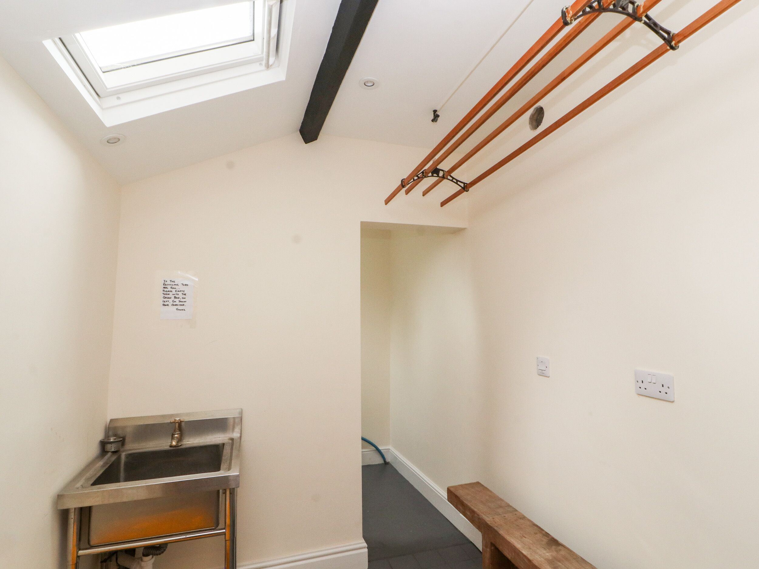 A narrow room with a skylight, a stainless steel sink, and a wooden bench.