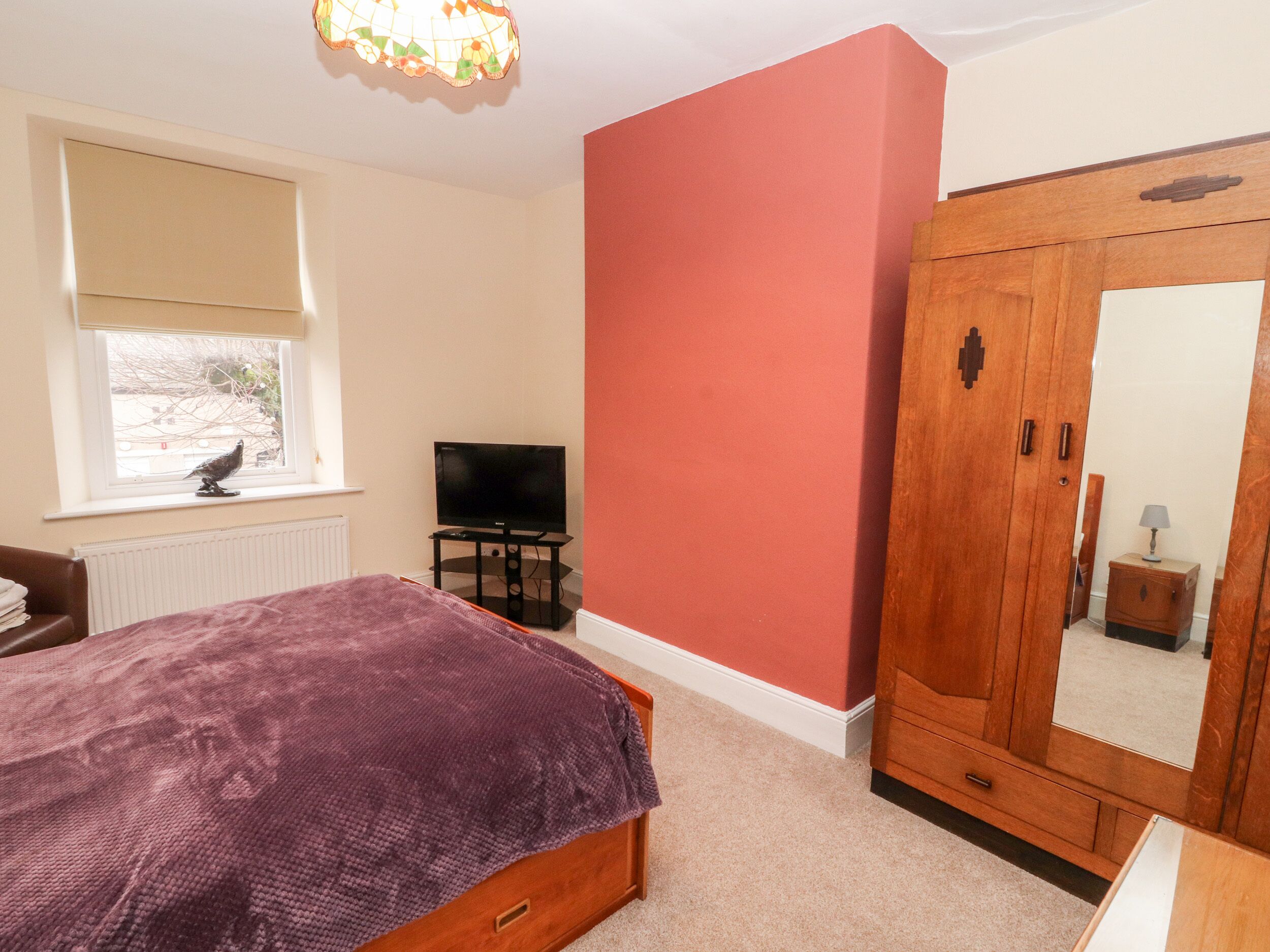 A bedroom with a bed, a television, a wardrobe, and a window with a bird outside.