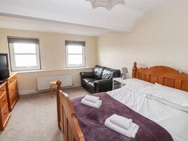 A bedroom with a bed, a wooden dresser, a black leather sofa, and two windows.