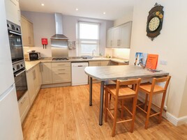 A modern kitchen with a central island, wooden chairs, and a wall-mounted clock.