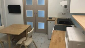 Pieni, käytännöllinen keittiönurkkaus, jossa on pieni jääkaappi, pesuallas ja mikroaaltouuni. Nurkkauksessa on myös puinen pöytä, jossa on kaksi tuolia, sekä seinälle asennettu televisio.