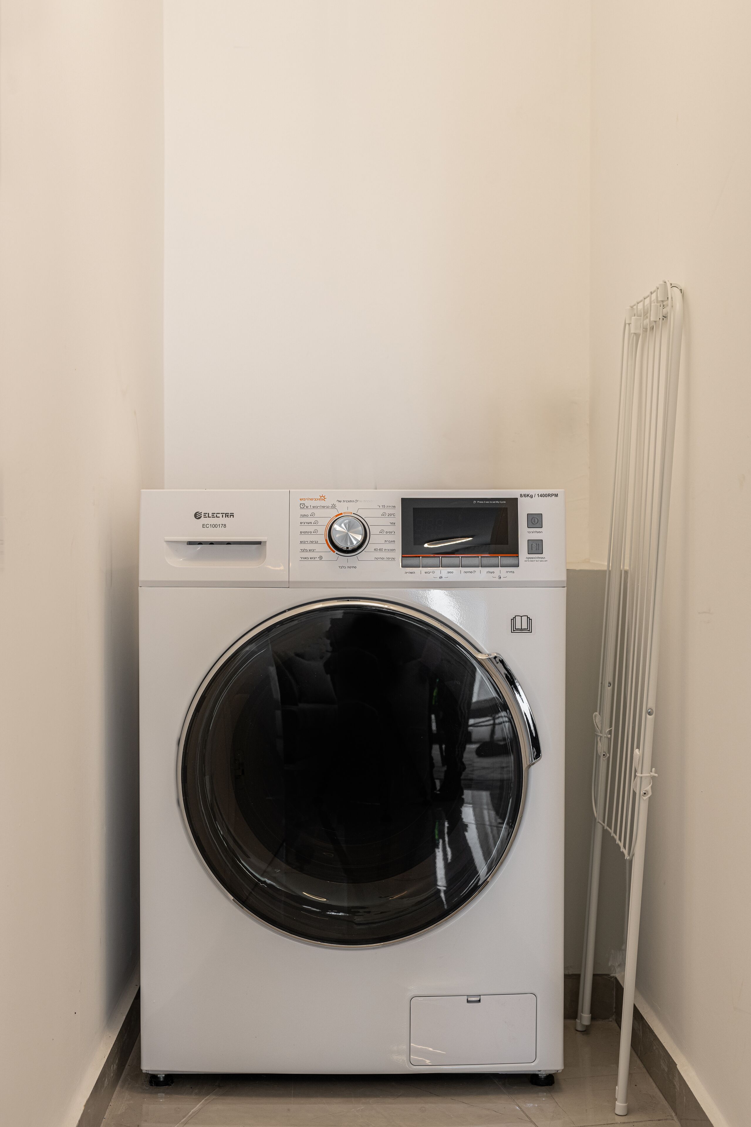 Lavadora de carga frontal en un cuarto de lavado, con panel de control y un respiradero en la pared.