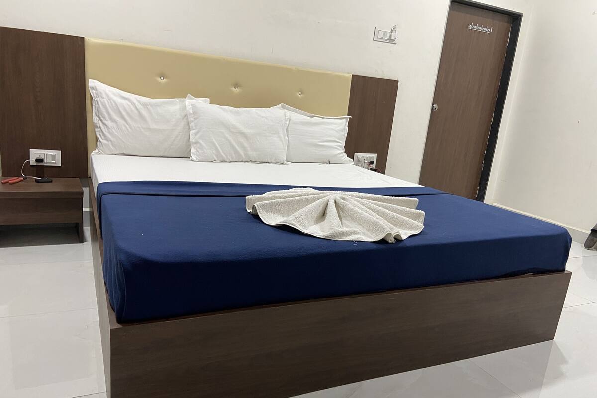 A neatly made bed with white pillows and a blue bedspread, a wooden nightstand with a phone and charger, and a door with a handle.