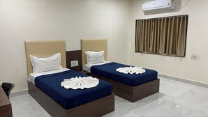 A hotel room with two beds, each with a headboard, a window with curtains, and an air conditioning unit on the wall. - Hotel Millennium Plaza (Jamnagar)