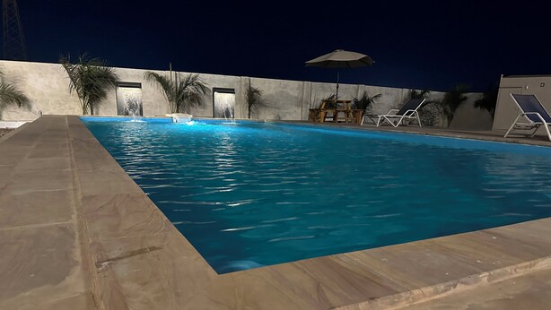 A swimming pool with a wooden deck, lounge chairs, and palm trees. - Hotel Millennium Plaza (Jamnagar)