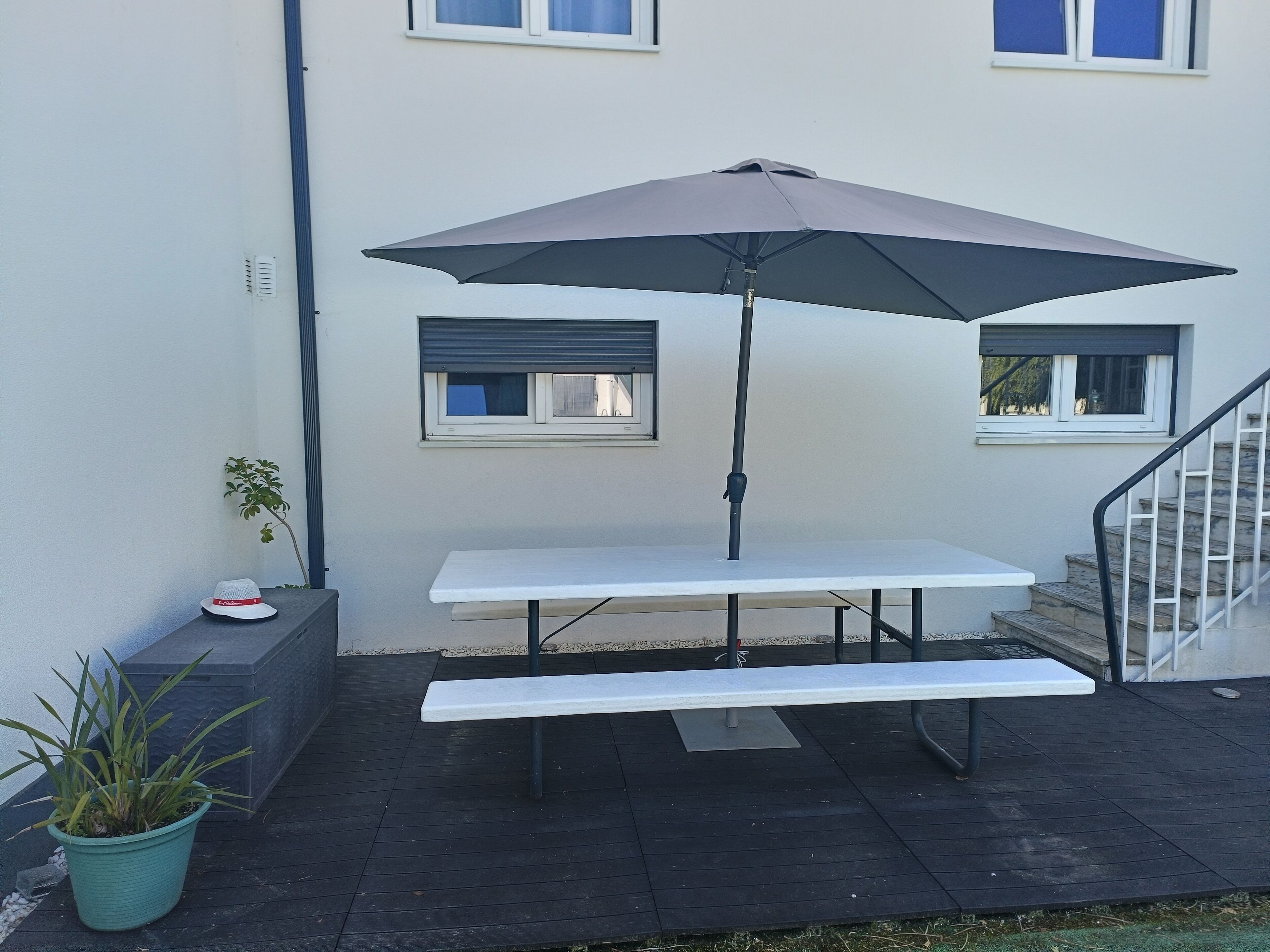 A patio with a table and an umbrella, a potted plant, and a staircase.