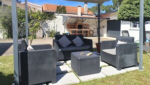 Un'area patio esterna con mobili in vimini, un barbecue e una zona salotto coperta.