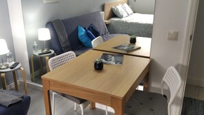 Una camera d'albergo compatta con un tavolo in legno, due sedie, una poltrona, un tavolino con una lampada e un letto con testiera.