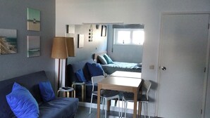 Una stanza compatta con un divano, un tavolino e un letto. Diverse immagini sono appese alle pareti e c'è un lampadario.