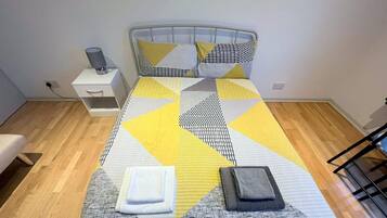 A bed with a geometric patterned bedspread, a bedside table with a lamp, and a chair.