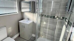 Ein modernes Badezimmer mit einer Duschkabine, einer Toilette, einem Waschbecken und einem Spiegel.