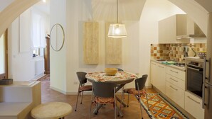 A kitchen with an arched ceiling, a round dining table with chairs, a hanging light fixture, and a tiled backsplash. - Siena UP Town: Sabrina's Lovely apartment (Siena)