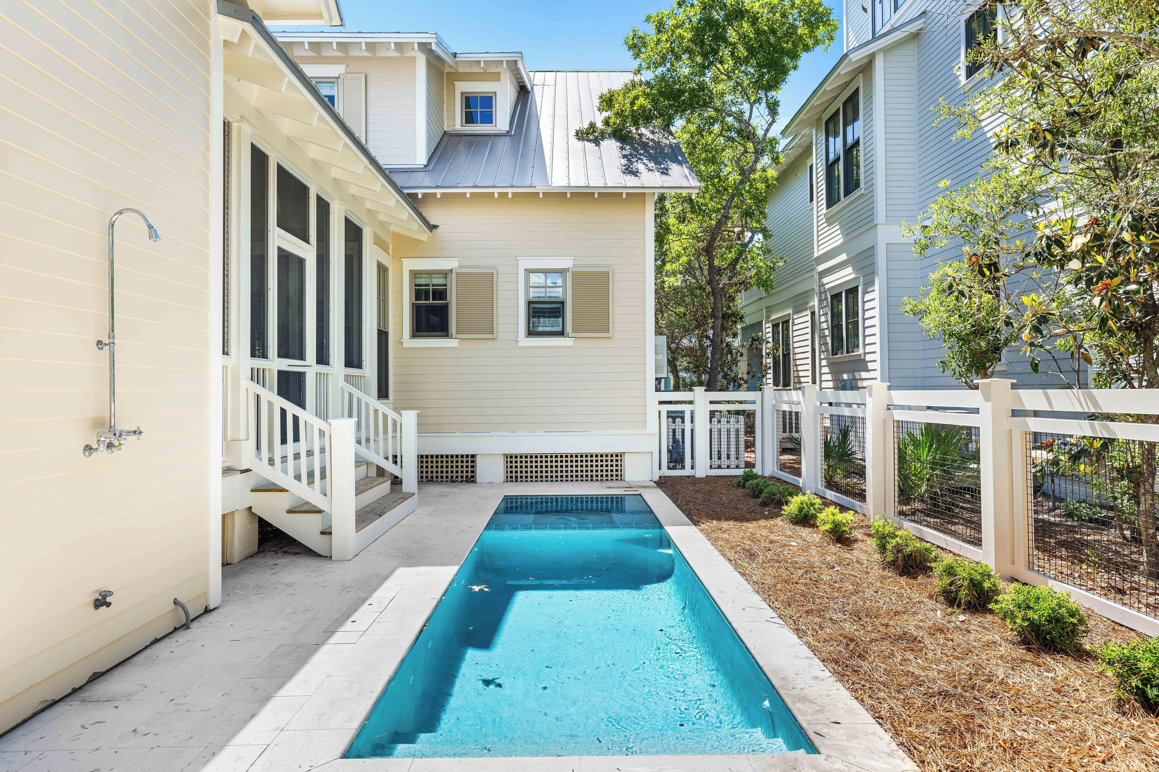 A swimming pool with a white deck, surrounded by a wooden fence and small plants.