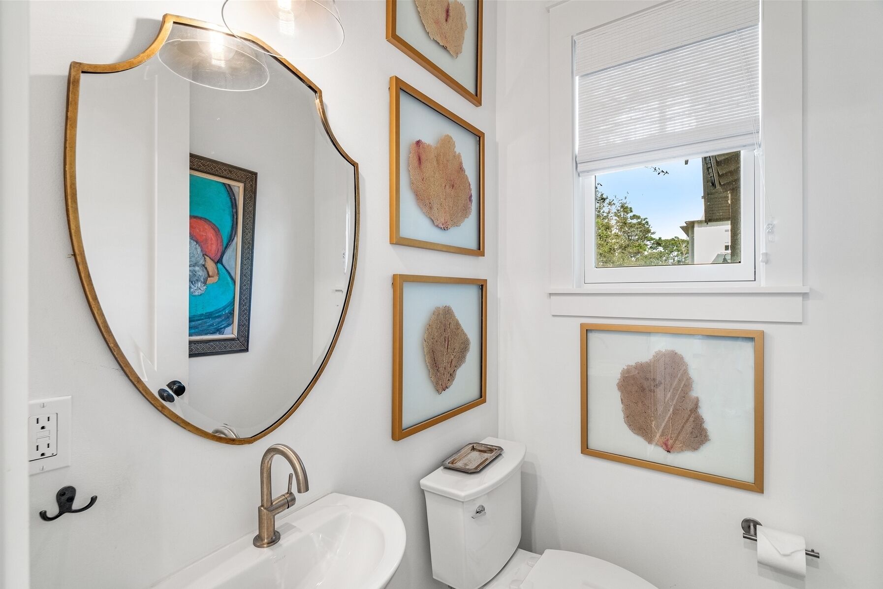 A bathroom with a white sink, a toilet, a mirror with a gold frame, and framed artwork on the wall.