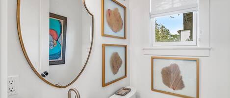 A bathroom with a white sink, a toilet, a mirror with a gold frame, and framed artwork on the wall.