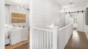 Un intérieur moderne avec un lambris blanc, un canapé blanc, un élément décoratif mural et un escalier avec une rampe blanche.