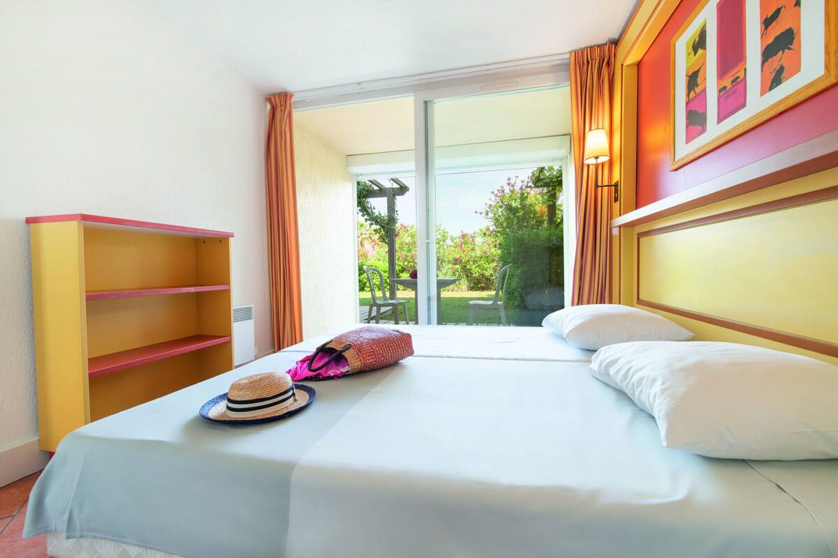 A hotel room with a bed, a wardrobe, a window with curtains, and a view of greenery outside.
