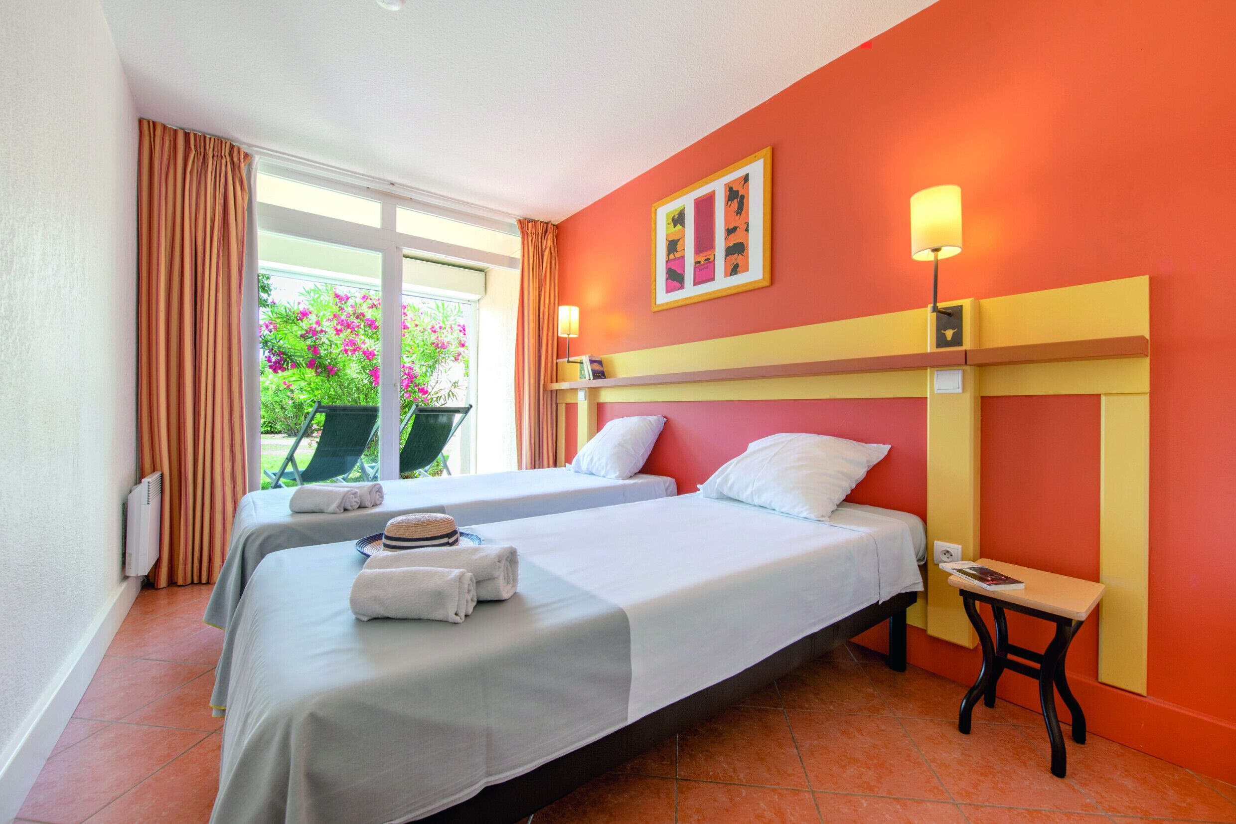 Habitación de hotel con dos camas, una ventana con cortinas, una silla cerca y una mesa con lámpara.