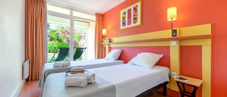 Habitación de hotel con dos camas, una ventana con cortinas, una silla cerca y una mesa con lámpara.