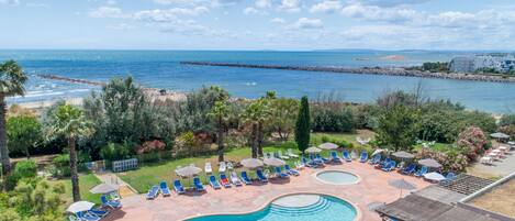 Un complexe hôtelier doté d’une piscine, de chaises longues et offrant une vue sur la mer.