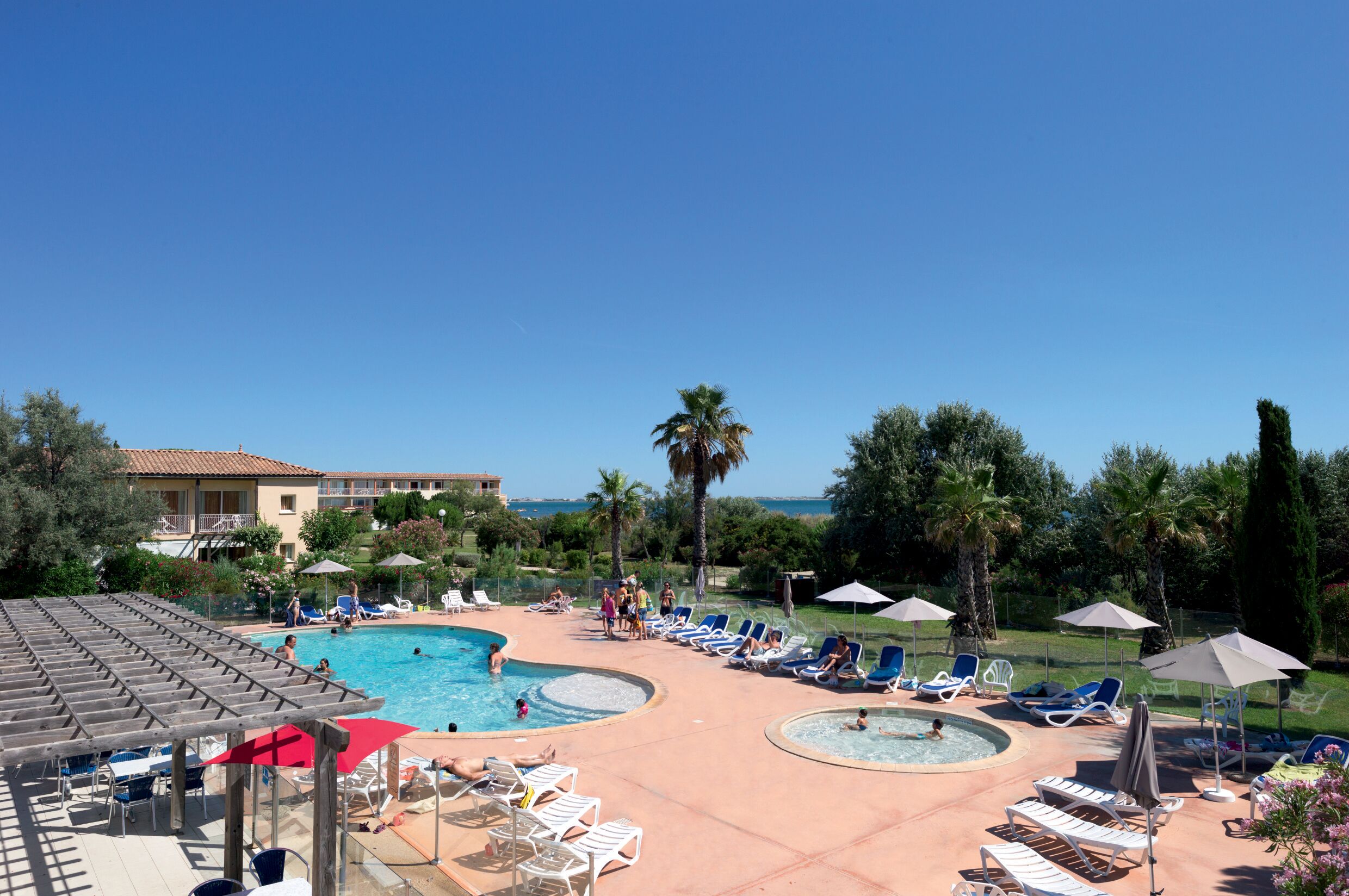 A pool area with multiple pools, lounge chairs, umbrellas, and a building in the background.