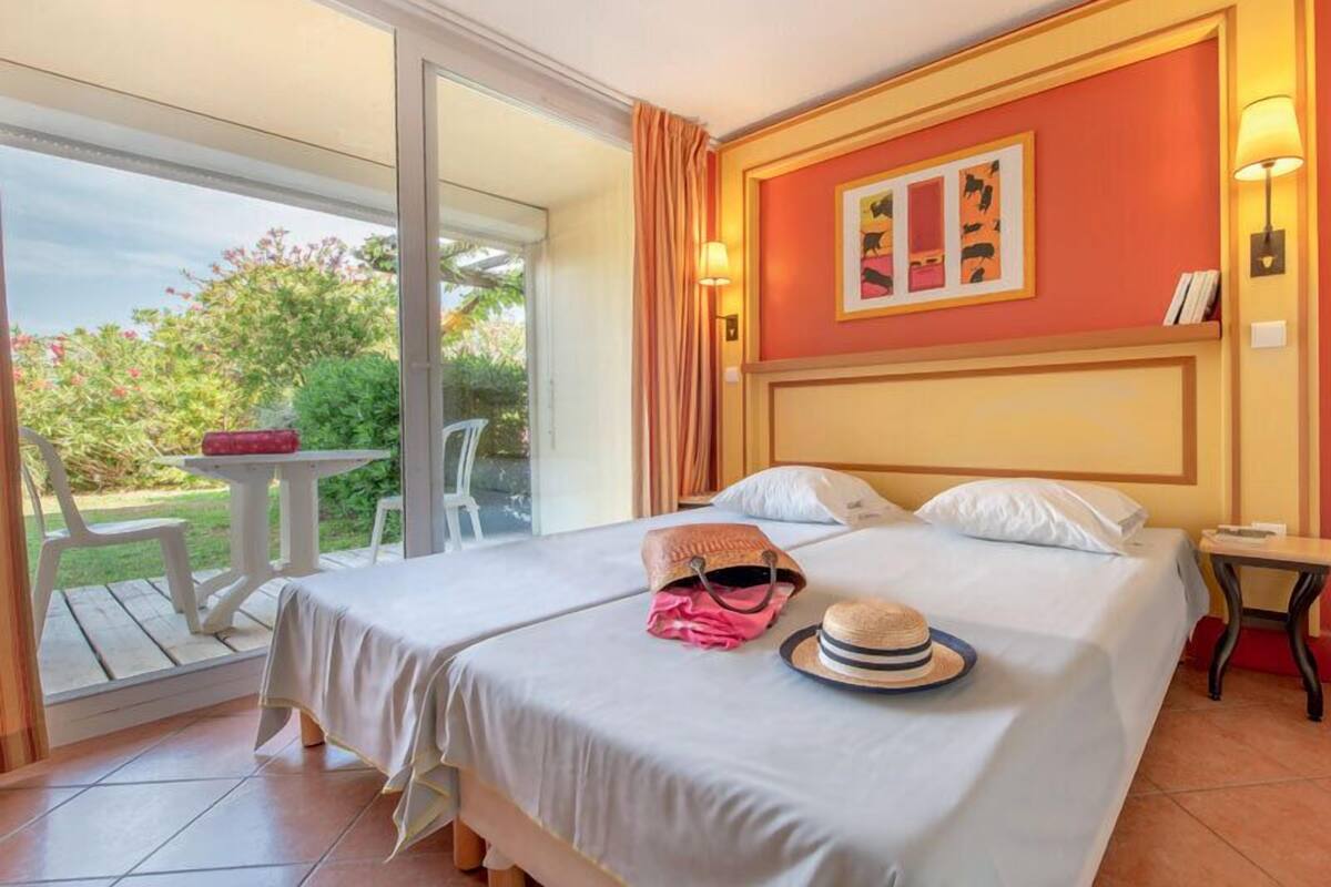 A hotel room with a bed, a table, and a chair outside the window.