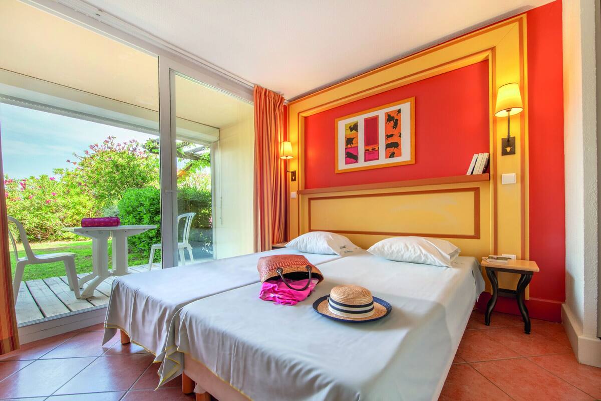A hotel room with a bed, a small table, a chair, and a view of the garden.
