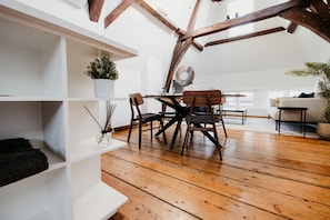 Un loft spacieux avec des poutres apparentes, un coin repas avec une table et des chaises, et un coin salon confortable avec un canapé.