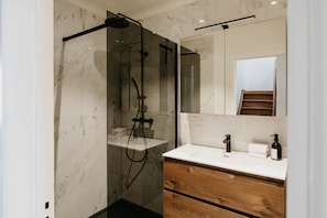 Une salle de bain moderne avec une douche à parois de verre, un lavabo blanc doté de meubles en bois et un grand miroir au-dessus du meuble-lavabo.
